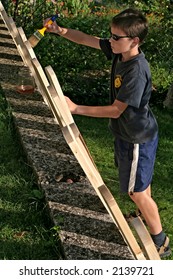 Teenager Boy Painting Planks For A Fence