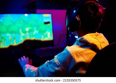 Teenager boy play computer video game in dark room, use neon colored rgb mechanical keyboard, place for cybersport gaming
