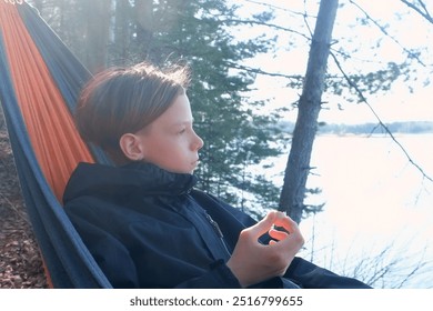 Teenager boy relaxing lying in hammock eating sausage in forest on nature. Resting relaxed brunet teen enjoying time in camping in woodland. Tourist, traveler, camper contemplating outdoors. - Powered by Shutterstock