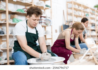 Teenager boy sculpts clay pottery on a potter wheel - Powered by Shutterstock