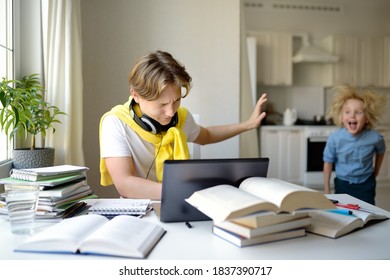 Teenager Boy Study At Home And His Younger Brother Screams And Interrupts Him. Online Education And Distance Learning For High School Students. School Boy Doing His Homework Using Gadgets.