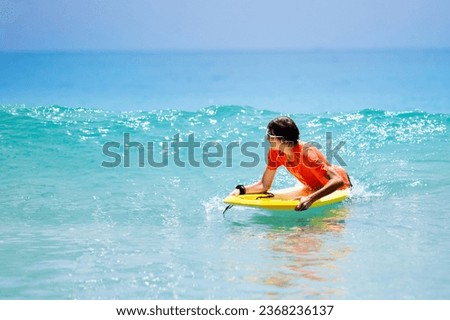 Teenager boy surfing on tropical beach in Asia. Child on surf board on ocean wave. Active water sports for kids. Kid swimming with body board. Young surfer in exotic sea. Swim and eye wear for kids.