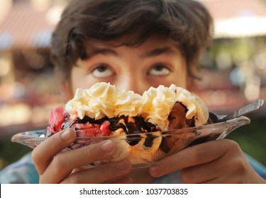 teenager boy sweet tooth eating Banana split sundae ice cream in a bowl funny grimace photo
