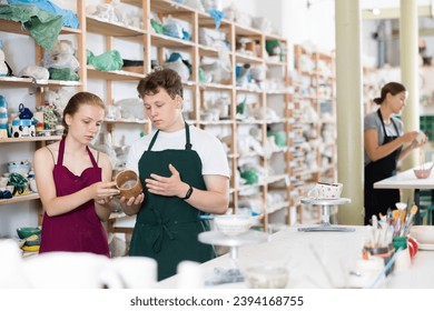 Teenager boy and teenage girl students in apron examining handmade ceramic cup in workshop - Powered by Shutterstock