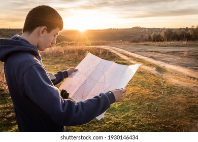 Teenager boy using map in the countryside and enjoying sunset. Selective focus. - Powered by Shutterstock