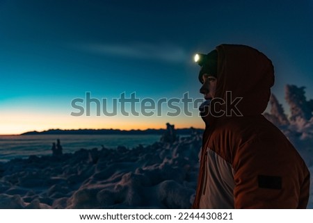 Teenager boy in a warm winter jacket with a headlamp on a mountain winter trail.