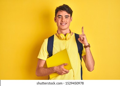 Teenager boy wearing headphones and backpack reading a book over isolated background surprised with an idea or question pointing finger with happy face, number one