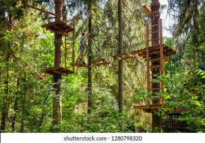 Teenager boy wearing safety harness passing rope bridge obstacle at a ropes course in outdoor treetop adventure park - Powered by Shutterstock