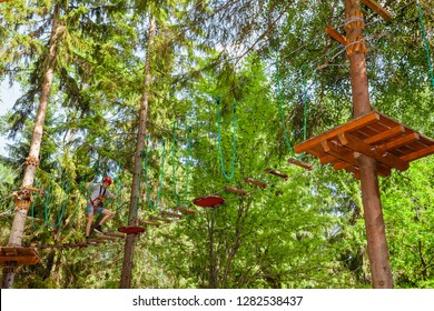 Teenager boy wearing safety harness passing hanging rope bridge obstacle at a ropes course in outdoor treetop adventure park - Powered by Shutterstock