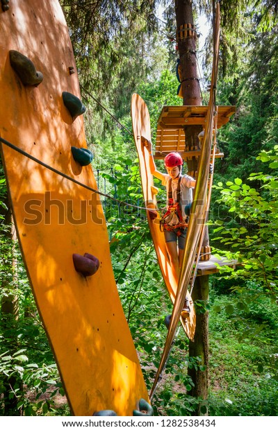 Teenager boy
wearing safety harness passing rope bridge obstacle at a ropes
course in outdoor treetop adventure
park