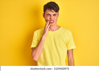 Teenager boy wearing yellow t-shirt over isolated background touching mouth with hand with painful expression because of toothache or dental illness on teeth. Dentist concept.