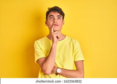 Teenager Boy Wearing Yellow T-shirt Over Isolated Background With Hand On Chin Thinking About Question, Pensive Expression. Smiling With Thoughtful Face. Doubt Concept.