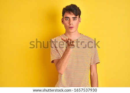 Teenager boy wearing yellow t-shirt over isolated background looking at the camera blowing a kiss with hand on air being lovely. Love expression.
