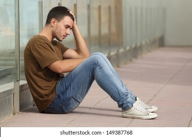 Teenager boy worried sitting on the floor with a hand on the head