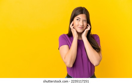 Teenager Brazilian girl over isolated yellow background frustrated and covering ears - Powered by Shutterstock