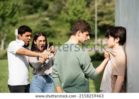 Teenager bully menacing boy while friends are recording. Bullying and violence at school concept