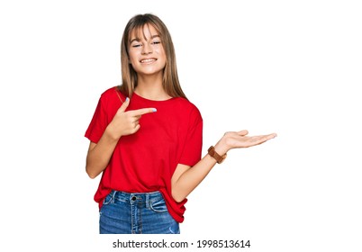 Teenager caucasian girl wearing casual red t shirt amazed and smiling to the camera while presenting with hand and pointing with finger. 