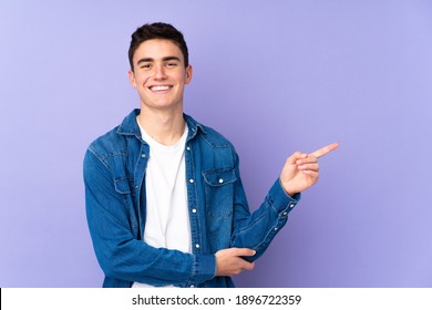 Teenager caucasian  handsome man isolated on purple background pointing finger to the side