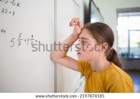 teenager child student solves an example problem with fractions on blackboard in school classroom in math algebra lesson. on face is bright emotion of surprise, difficulty.
