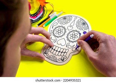 Teenager coloring with felt-tip pens wooden skull on yellow background. Day of the dead concept. Mexican traditional holiday. Selective focus - Shutterstock ID 2204935321