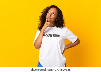 Teenager cuban volunteer girl isolated on yellow background having doubts while looking up
