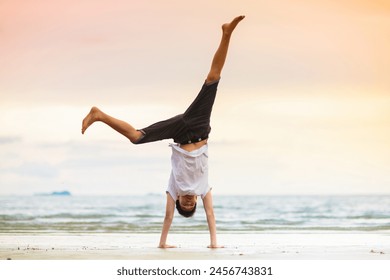 Teenager doing calisthenics exercise. Beach yoga at sunset. Teen boy exercising. Wheel and headstand pose training. Sport for active young adult man. Arm balance asana. School child sports. - Powered by Shutterstock