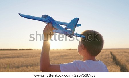 Teenager dreams of flying becoming pilot. Kid aviator. Happy child throws toy plane with his hand on field, sunset. Boy child wants to become pilot, astronaut. Slow motion. Children play toy airplane
