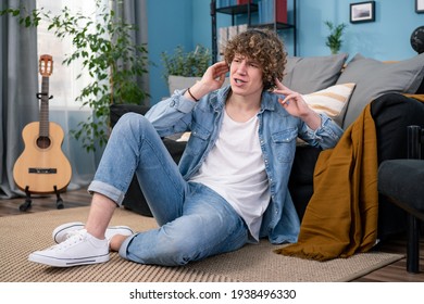 A Teenager Dressed In Jeans Pants And Shirt Is Hanging Out In The Living Room At Home. The Boy Is Watching A Concert Of His Favorite Band On TV And Listening To Their Music On Headphones.