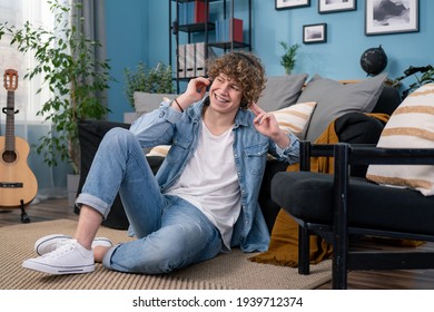 A Teenager Dressed In Jeans Pants And Shirt Is Hanging Out In The Living Room At Home. The Boy Is Watching A Concert Of His Favorite Band On TV And Listening To Their Music On Headphones.