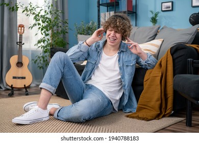 A Teenager Dressed In Jeans Pants And Shirt Is Hanging Out In The Living Room At Home. The Boy Is Listening A Concert Of His Favorite Band On Headphones. He Is Singing.