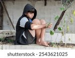 A teenager dressed in shorts and a gray-and-black hooded robe sat secluded in a dirty room, his face gloomy and sad because he was escaping from family problems and punishment from his parents.