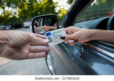 Teenager driver commited a minor offence and handing over her licence to a police officer reaching towards the open window.Police officer controlling traffic on the road - Shutterstock ID 2175831625