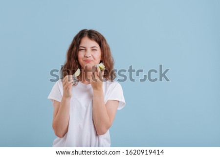 teenager eat slice of lime, make grimaces, in studio, isolated on blue background, copy space