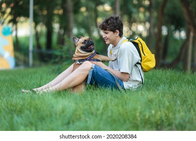 Teenager Embraces His Red French Bulldog Outside. Boy Walking With Cute Bulldog In The Park. Still Life, Friendship, Companionship With A Dog