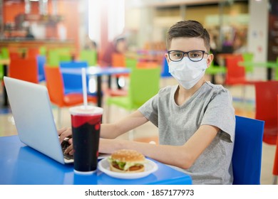 A Teenager In A Face Mask With A Laptop At Lunch In A Food Court Looks At The Camera