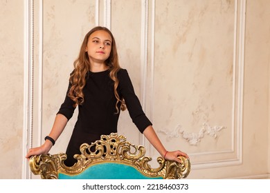 Teenager girl 12-13 year old with long hair, standing at armchair, looking away, fashion model in stylish black elegant dress in living room. Fashionable teen lady actress. Copy text space - Powered by Shutterstock