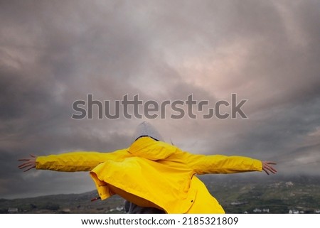 Teenager girl back to camera. Hands up in the air, Her jacket if lifted by a strong wind. Stormy sky in the background. Be strong no matter what concept.