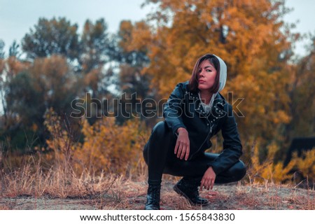 teenager girl in black leather clothes crouched on a background of yellow autumn forest