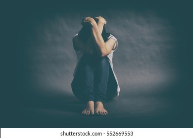 Teenager girl with depression sitting alone on the floor in the dark room. Toned photo