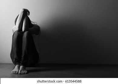 Teenager girl with depression sitting alone on the floor in the dark room.  Black and white photo