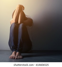Teenager girl with depression sitting alone on the floor in the dark room. Toned