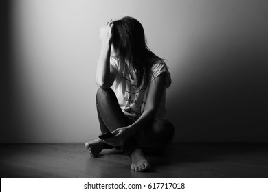 Teenager girl with depression sitting alone on the floor in the dark room.  Black and white photo 