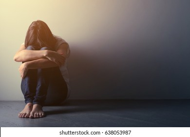 Teenager girl with depression sitting alone on the floor in the dark room. Toned photo 