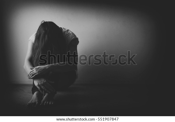 Teenager girl with depression\
sitting alone on the floor in the dark room. Black and white\
photo
