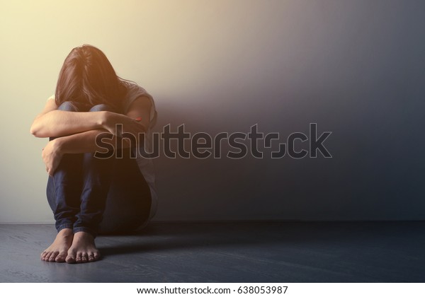 Teenager girl with depression sitting alone\
on the floor in the dark room. Toned photo\
