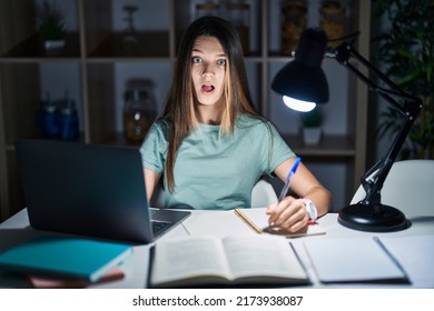 Teenager Girl Doing Homework At Home Late At Night In Shock Face, Looking Skeptical And Sarcastic, Surprised With Open Mouth 