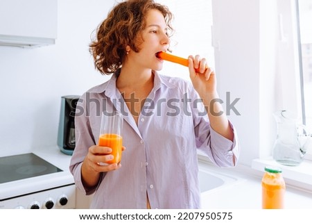 teenager girl eats fresh carrots with pleasure and holds carrot juice in glass in hand. Healthy proper nutrition, dietary breakfast, vitamins to improve vision. vitamin A for good vision
