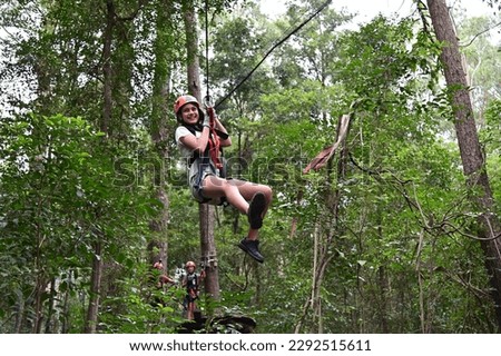 Teenager girl (female age 12) sliding on a flying fox zip line during a treetop adventure climbing. Girls power, risk and challenge concept. Real people. Copy space
