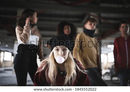 Teenager girl with friends standing indoors in abandoned building, making bubble gum.