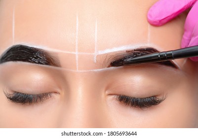 teenager girl having permanent makeup tattoo on her eyebrows. Make-up artist makes markings with white paste for eyebrow tattooing. Professional makeup and skin care cosmetology.